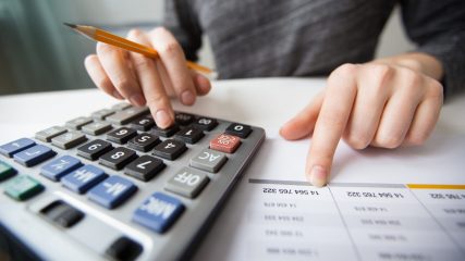 Closeup of accountant counting on calculator and working with table
